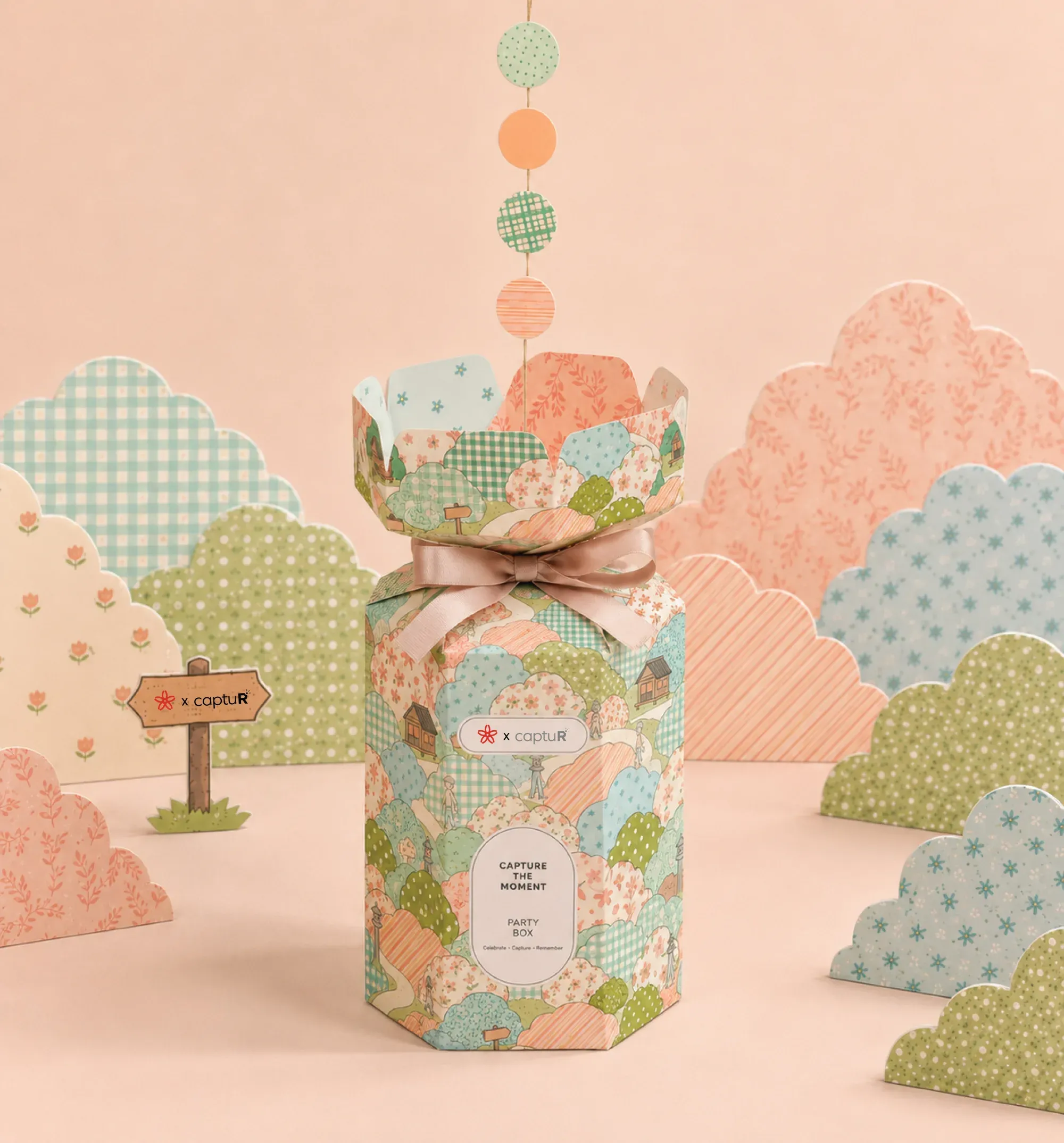 A pastel hexagonal captuR party box tied with a ribbon, styled among paper decorations.