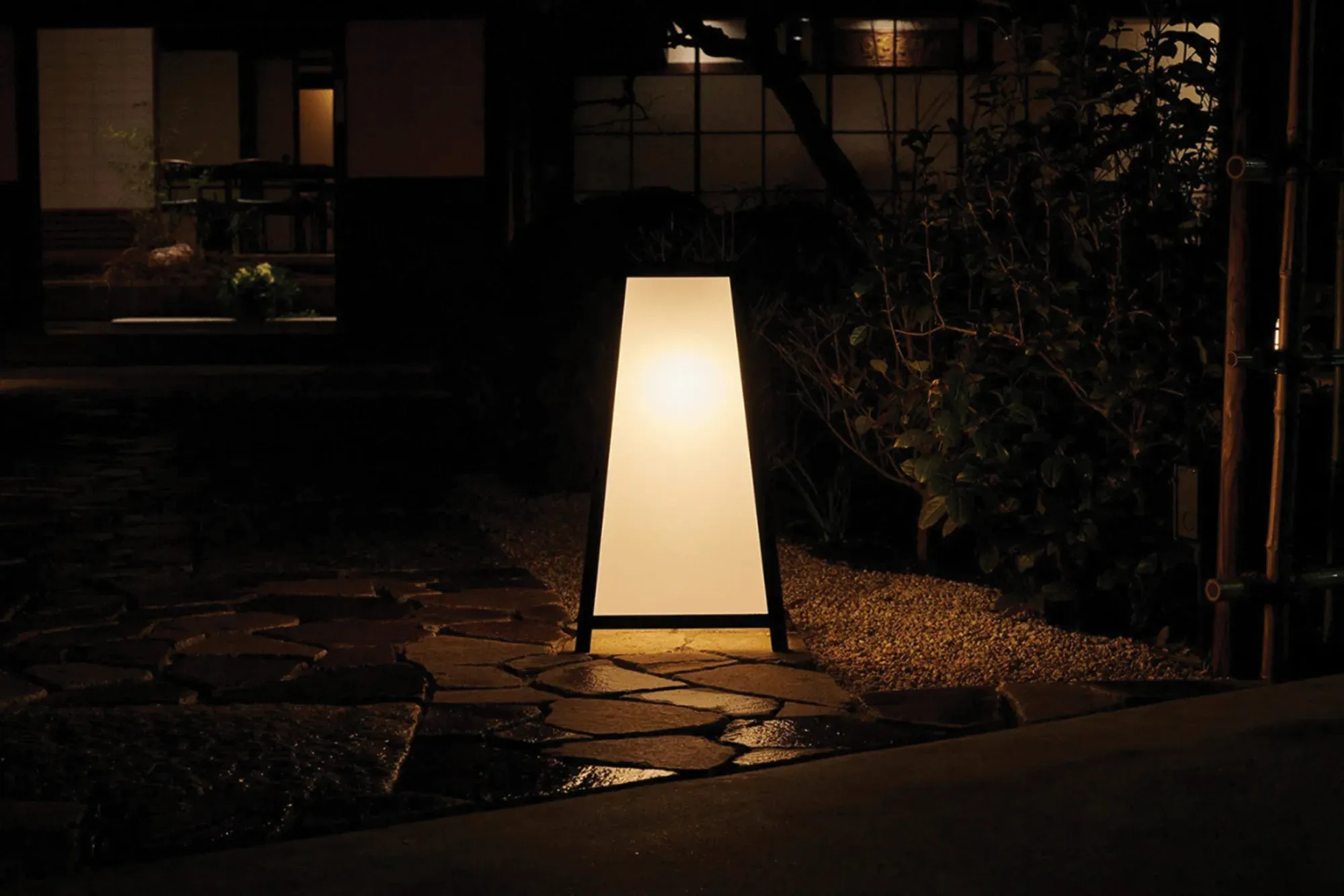 An illuminated lantern-style GINZA signage stand outside a dark traditional entrance at dusk.