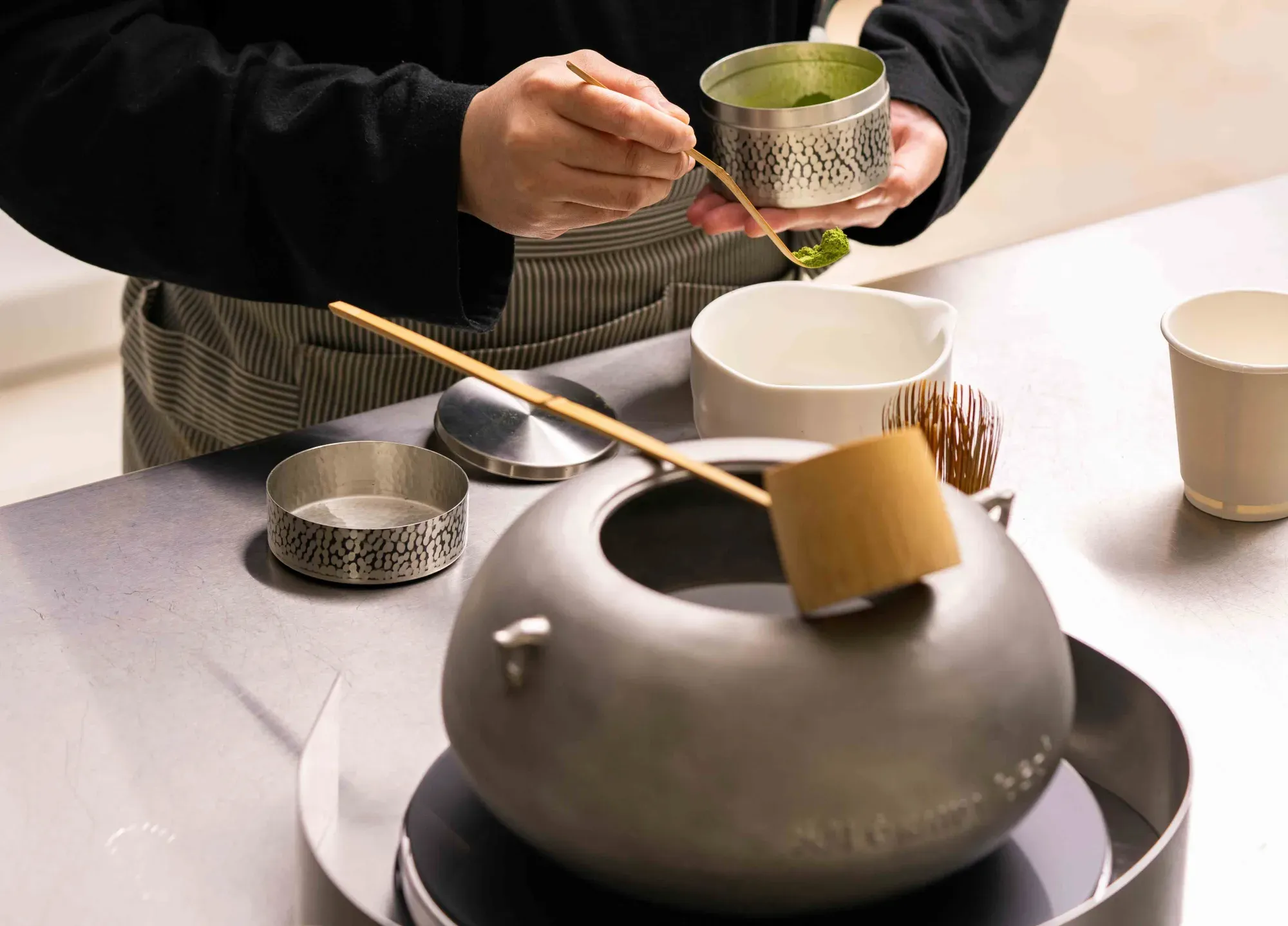 A hand whisking matcha in a bowl with a bamboo whisk on a tea-ceremony table setting.