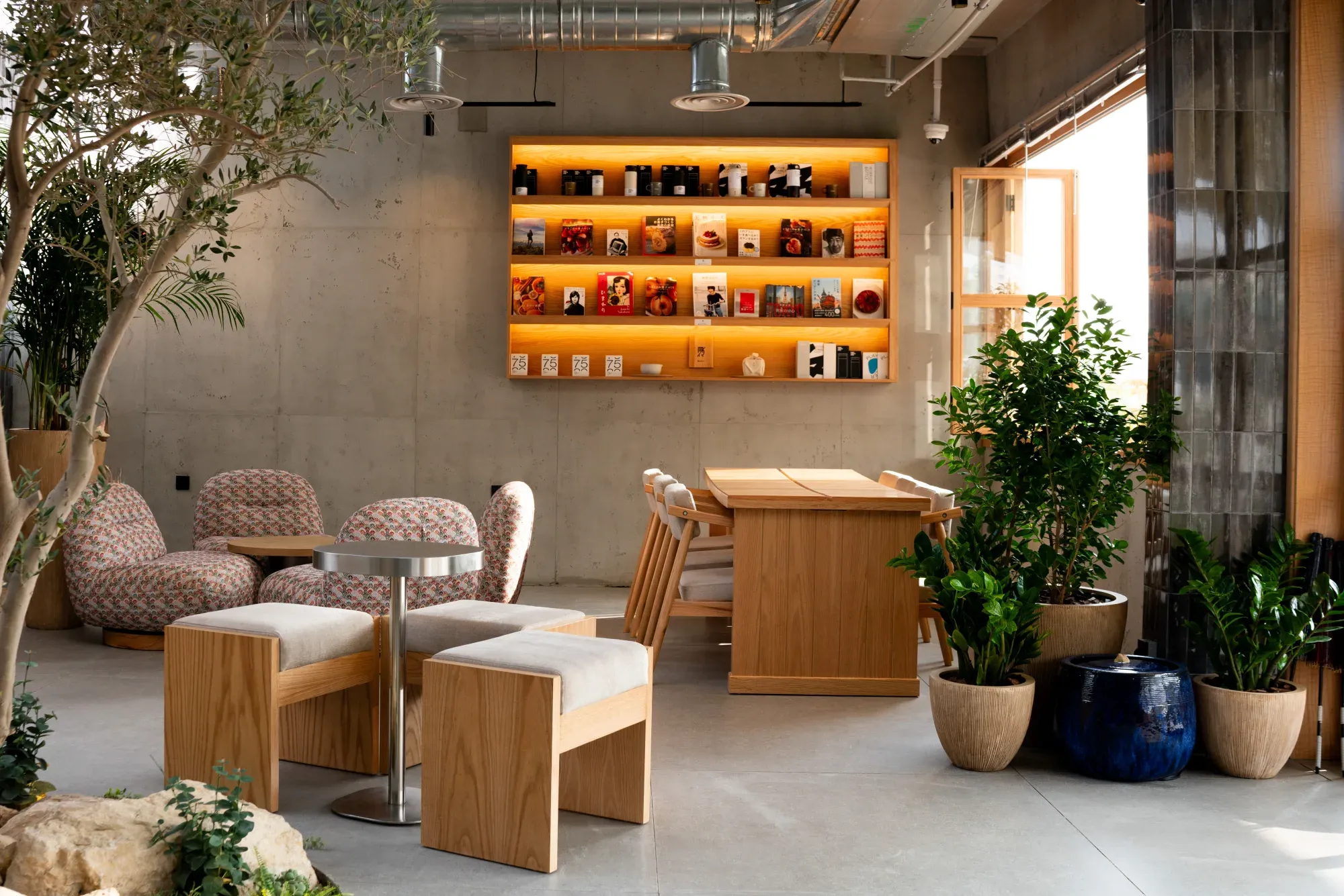 The ŌKAWA café lounge in Riyadh — backlit wood shelving stocked with books and packaged goods, patterned armchairs and a wood dining table.